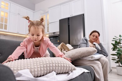 Tired housewife with her little daughter among messy laundry on sofa at home