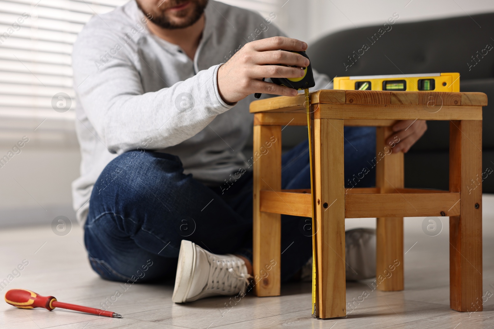 Photo of Man using level tool while repairing wooden stool at home, closeup