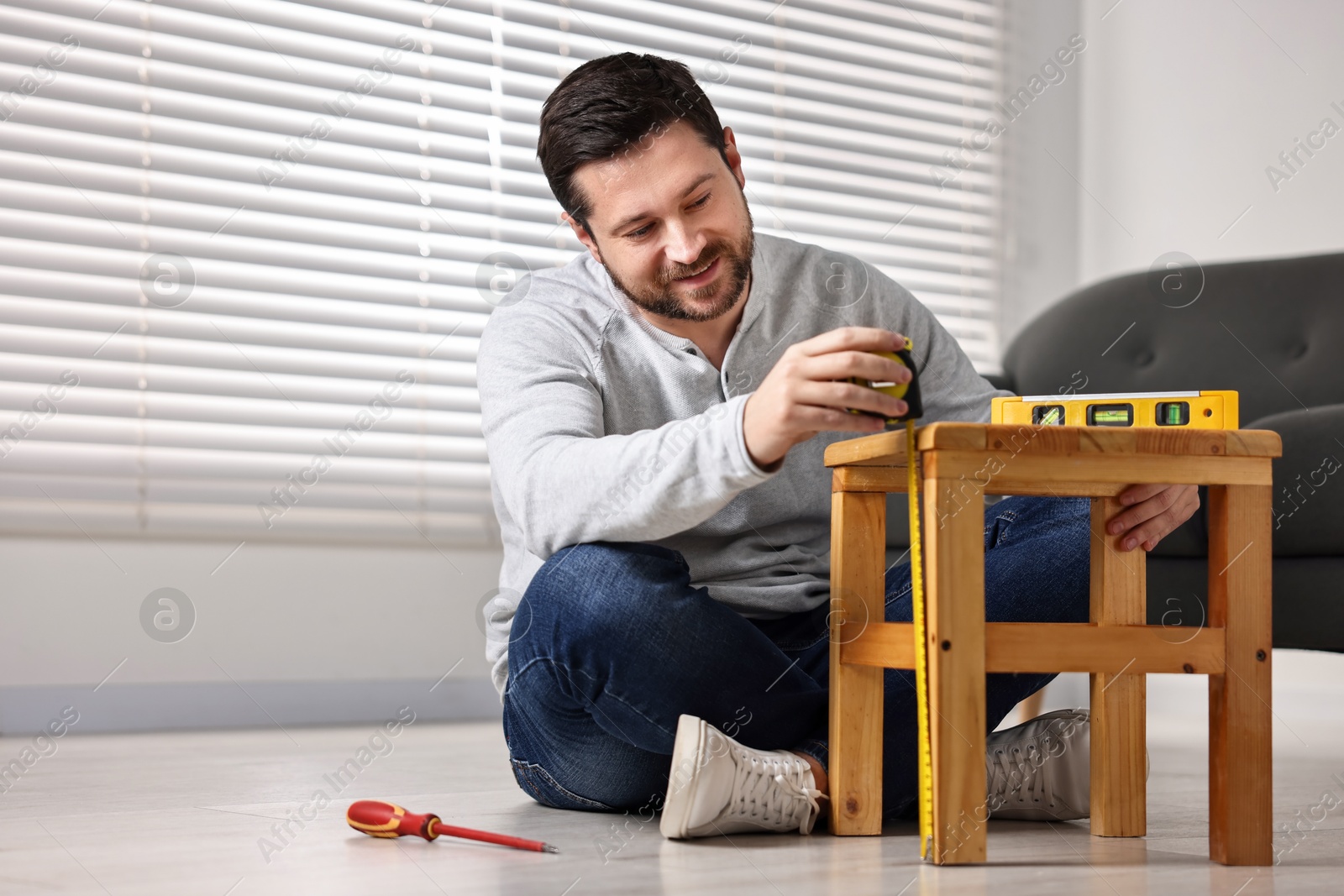 Photo of Man using level tool while repairing wooden stool at home