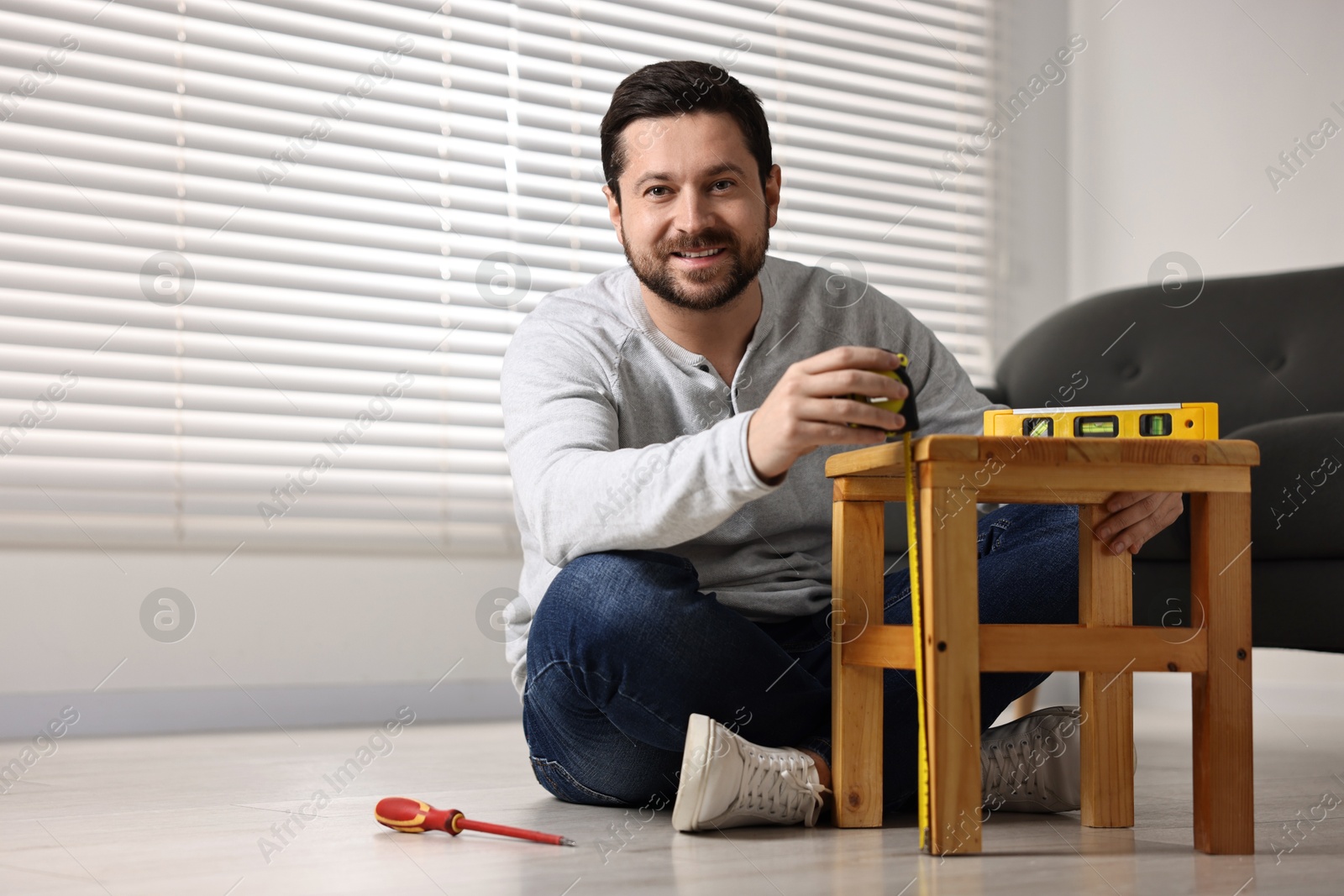 Photo of Man using level tool while repairing wooden stool at home