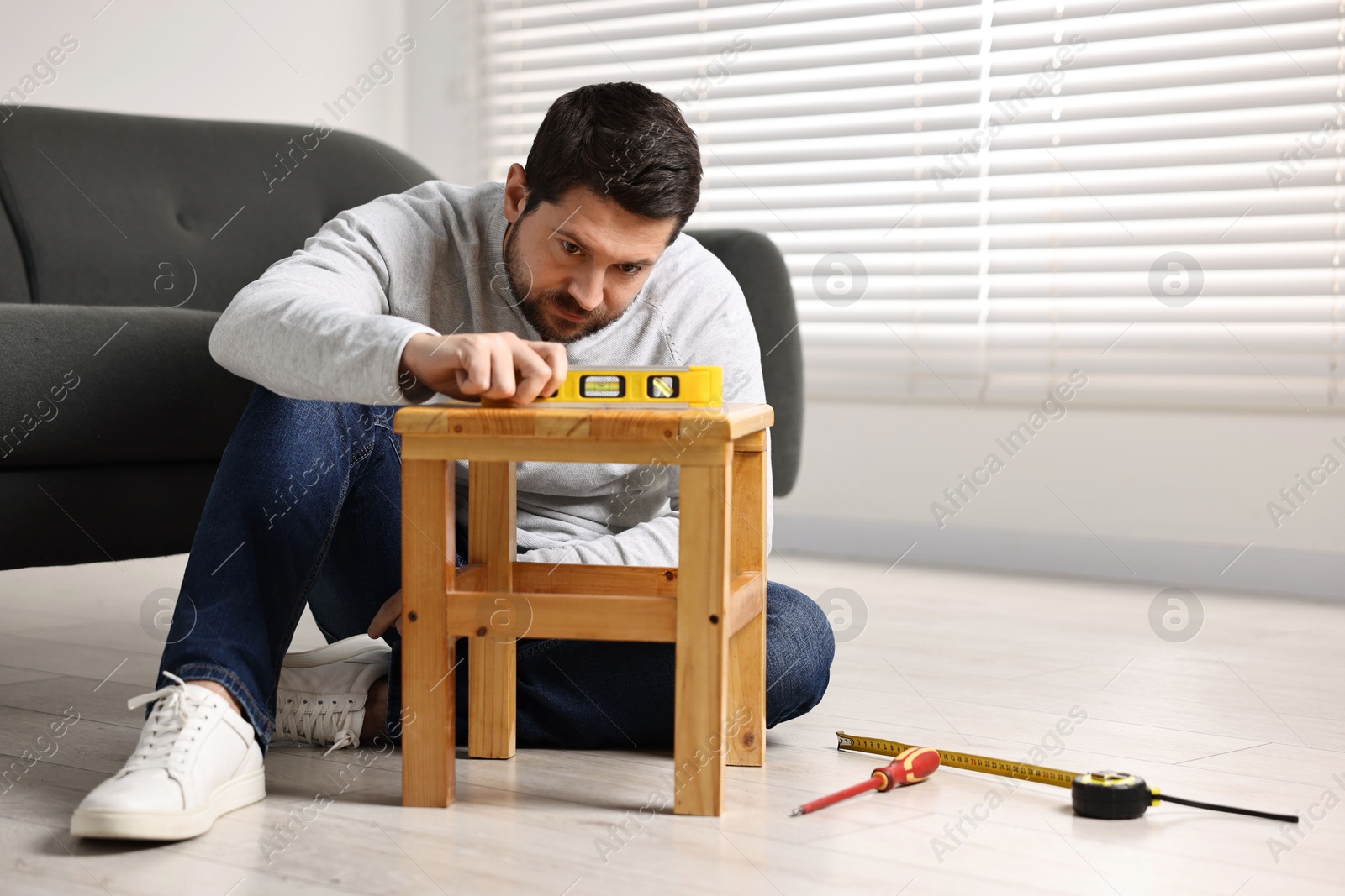 Photo of Man using level tool while repairing wooden stool at home