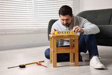 Photo of Man using level tool while repairing wooden stool at home