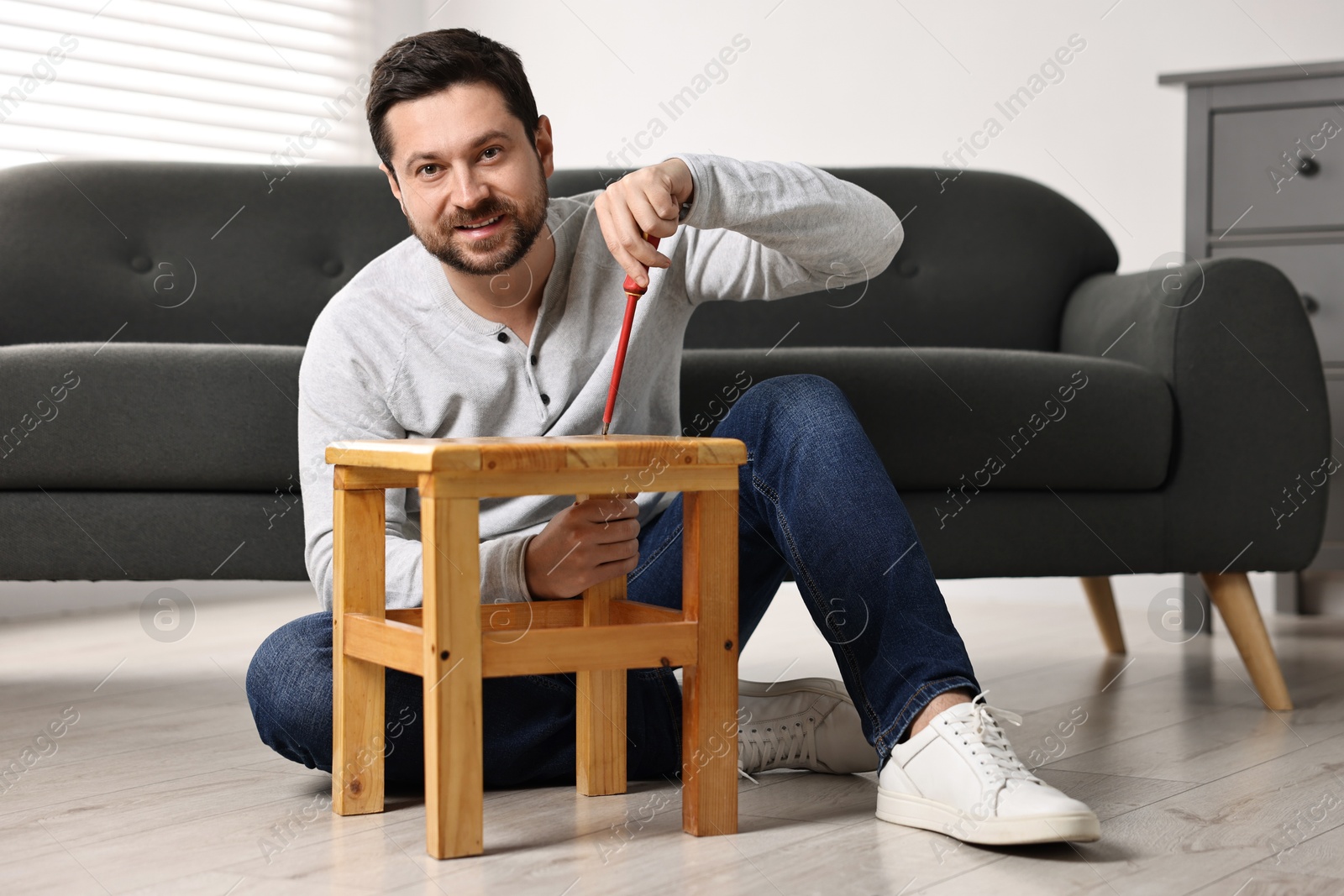 Photo of Man repairing wooden stool with screwdriver at home