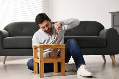 Photo of Man repairing wooden stool with screwdriver at home