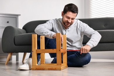 Photo of Man repairing wooden stool with screwdriver at home