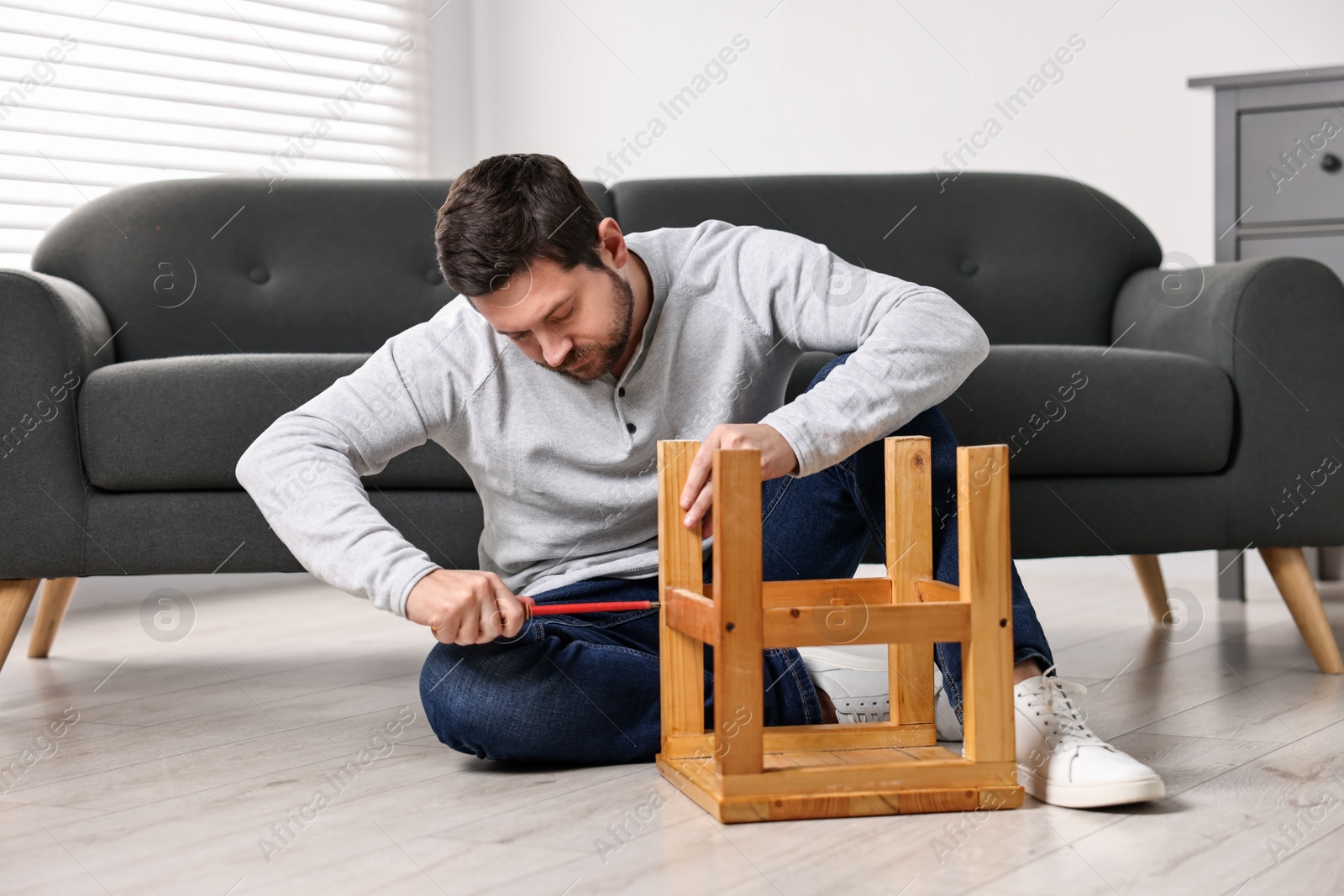 Photo of Man repairing wooden stool with screwdriver at home