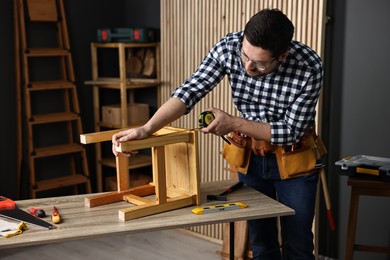 Photo of Repairman measuring wooden stool at table in workshop