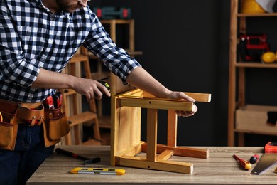 Photo of Repairman measuring wooden stool at table in workshop, closeup