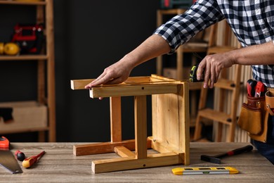 Photo of Repairman measuring wooden stool at table in workshop, closeup