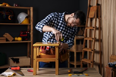 Photo of Repairman measuring wooden stool at table in workshop