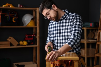 Photo of Professional repairman measuring wooden stool in workshop