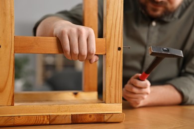 Photo of Man repairing wooden stool with nail and hammer at home, closeup