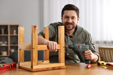 Photo of Man repairing wooden stool with electric screwdriver at home