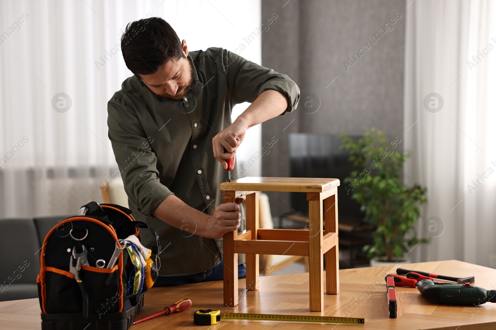 Photo of Man repairing wooden stool with screwdriver at home