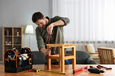 Photo of Man repairing wooden stool with screwdriver at home