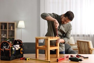 Photo of Man repairing wooden stool with screwdriver at home