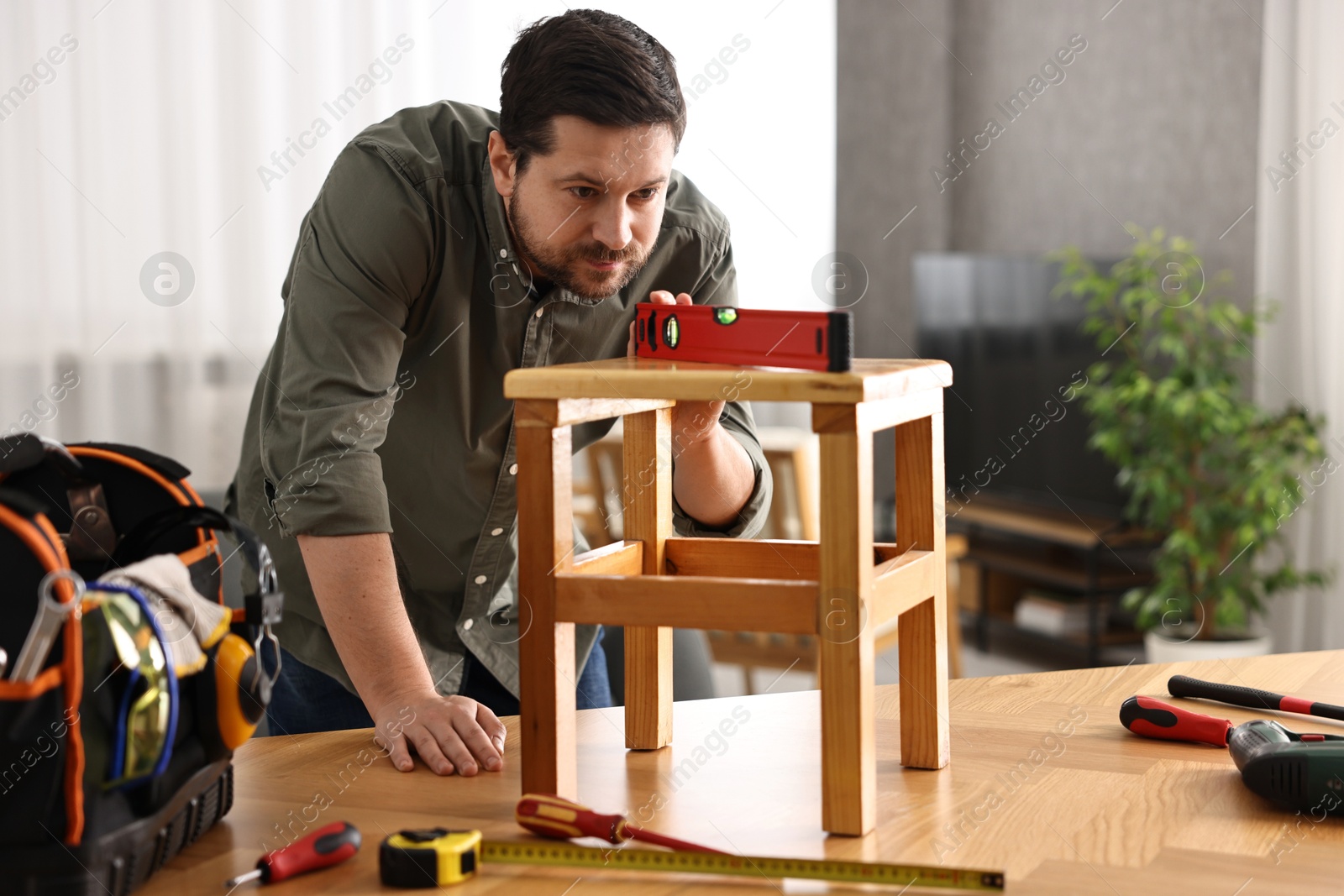 Photo of Man using level tool while repairing wooden stool at home