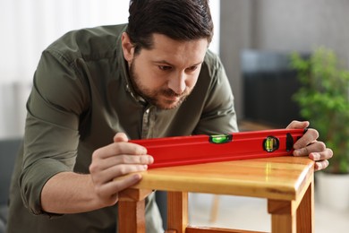 Man using level tool while repairing wooden stool at home