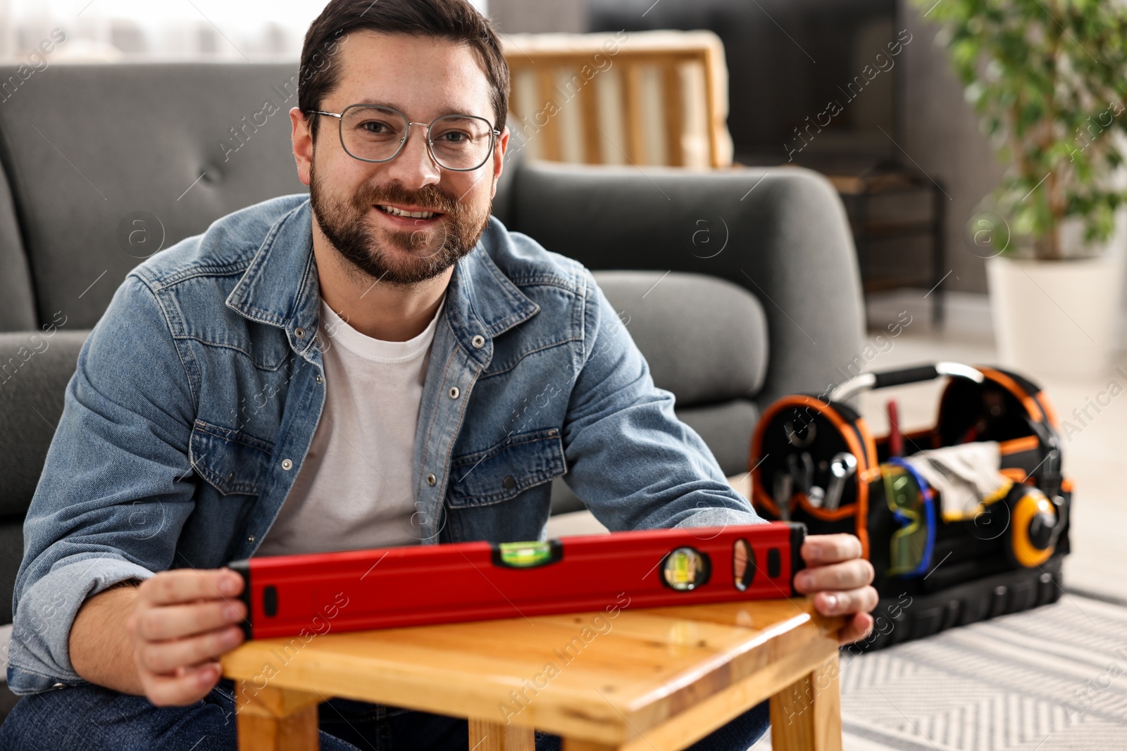 Photo of Man using level tool while repairing wooden stool at home