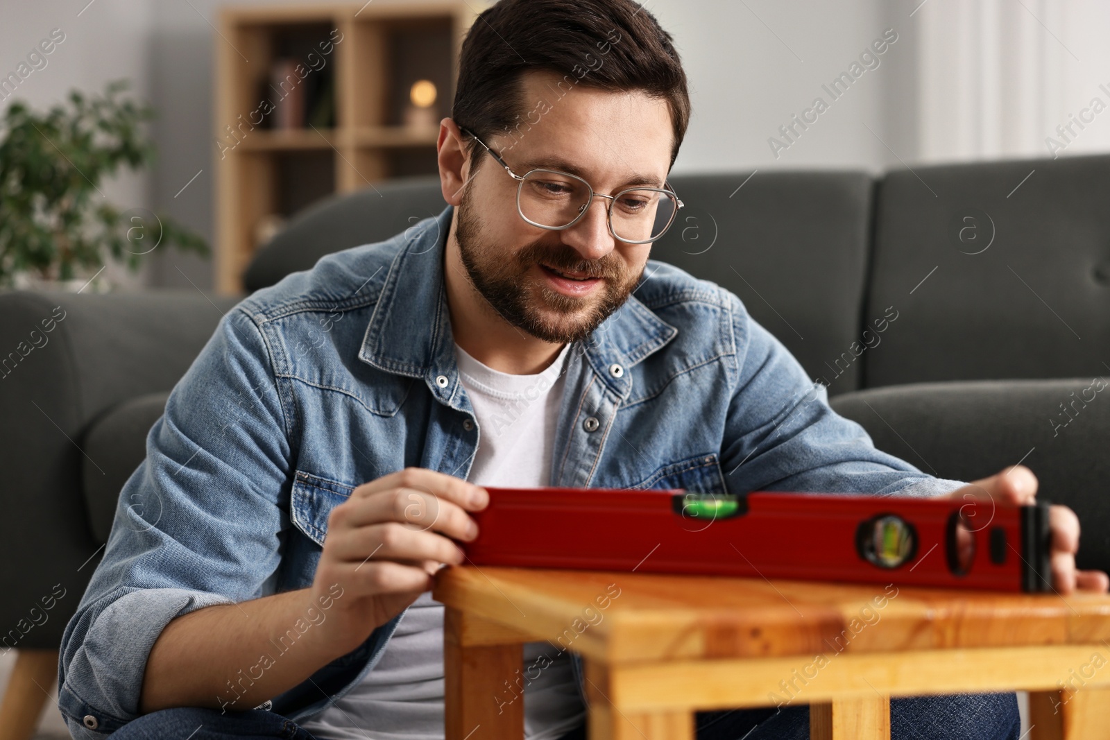 Photo of Man using level tool while repairing wooden stool at home