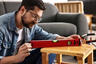 Photo of Man using level tool while repairing wooden stool at home