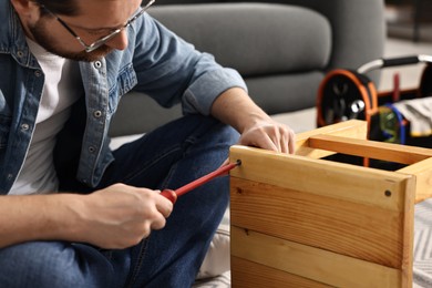 Photo of Man repairing wooden stool with screwdriver at home, closeup