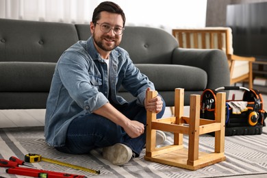 Man repairing wooden stool with screwdriver at home