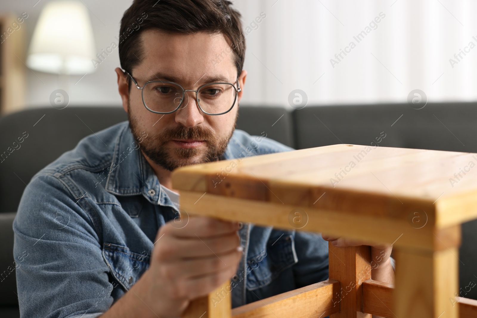 Photo of Man repairing wooden stool at home, selective focus