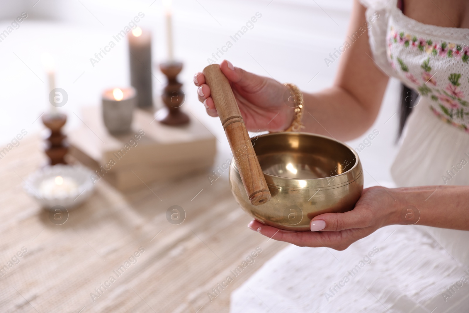 Photo of Woman with singing bowl and burning candles indoors, closeup