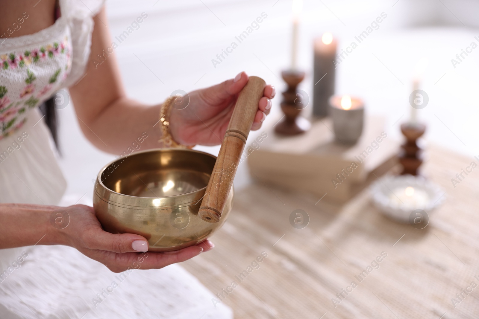 Photo of Woman with singing bowl and burning candles indoors, closeup