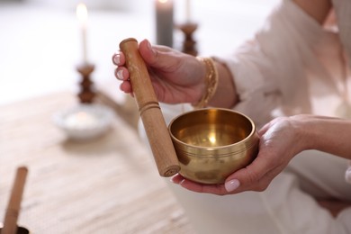 Photo of Woman with singing bowl and burning candles indoors, closeup