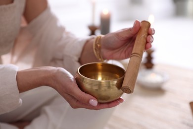 Photo of Woman with singing bowl and burning candles indoors, closeup