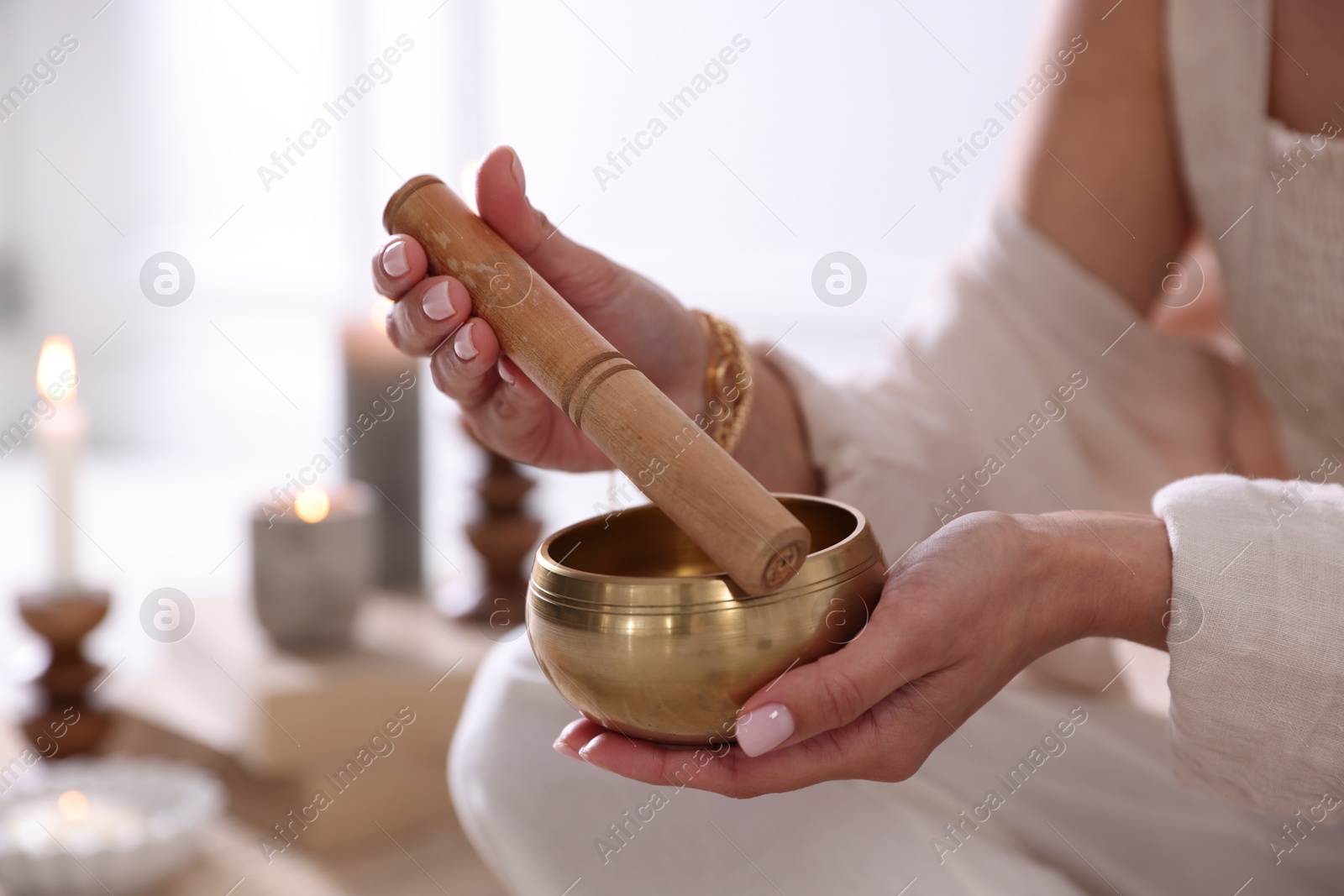 Photo of Woman with singing bowl and burning candles indoors, closeup