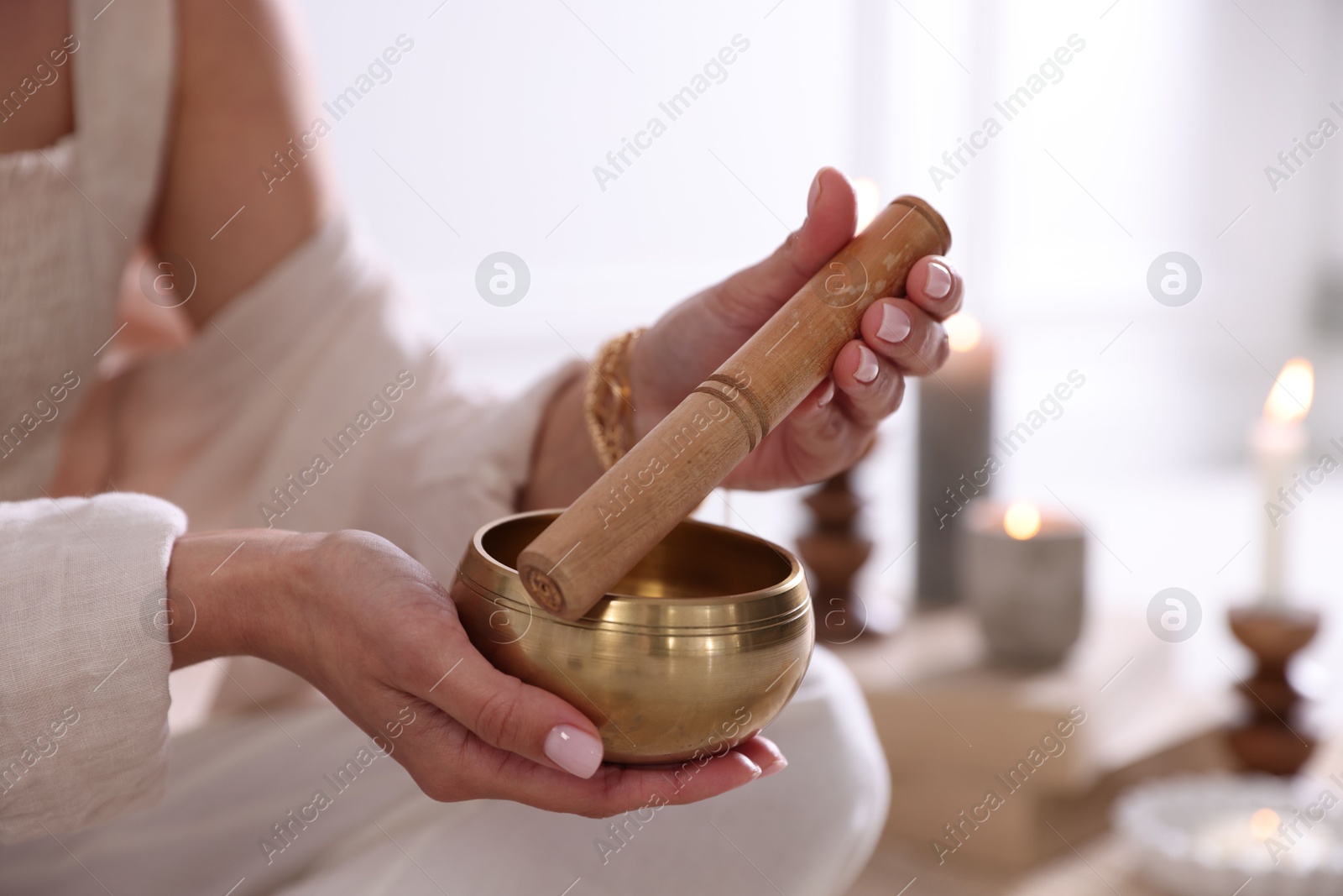 Photo of Woman with singing bowl and burning candles indoors, closeup