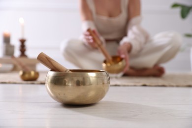 Photo of Woman with singing bowls on floor indoors, selective focus