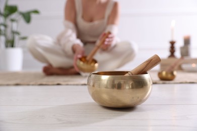 Photo of Woman with singing bowls on floor indoors, selective focus