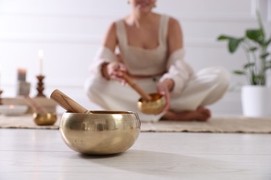 Photo of Woman with singing bowls on floor indoors, selective focus