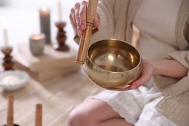 Photo of Woman with singing bowl and burning candles indoors, closeup