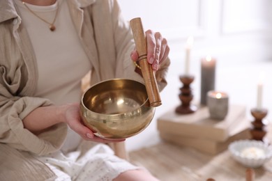 Photo of Woman with singing bowl and burning candles indoors, closeup