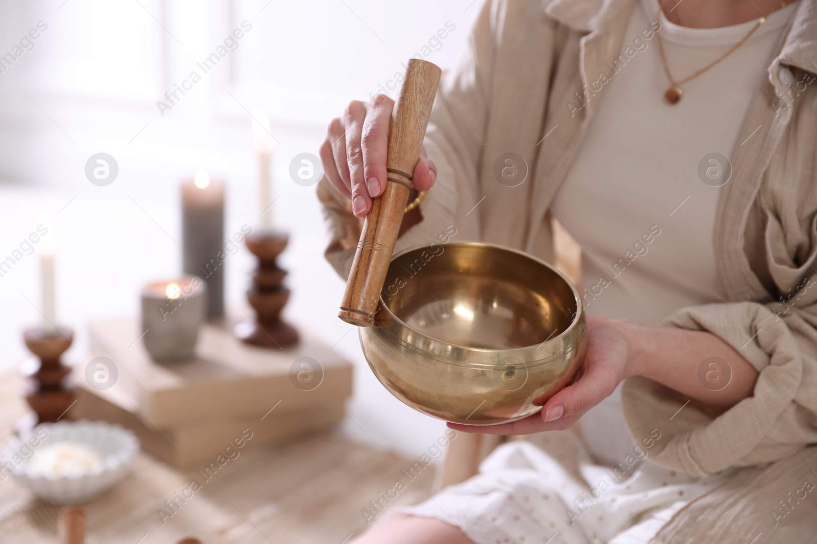 Photo of Woman with singing bowl and burning candles indoors, closeup