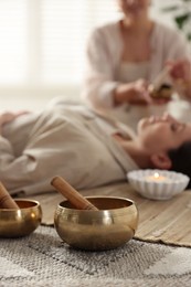 Woman undergoing singing bowl therapy indoors, selective focus