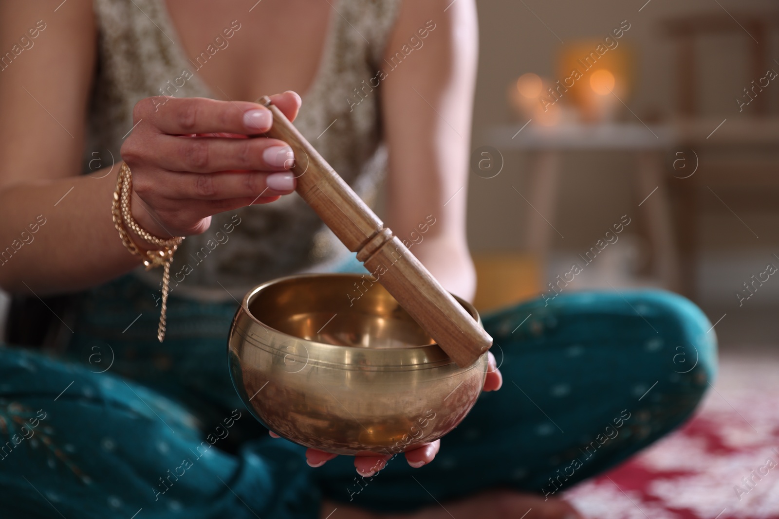 Photo of Woman with singing bowl and burning candles indoors, closeup