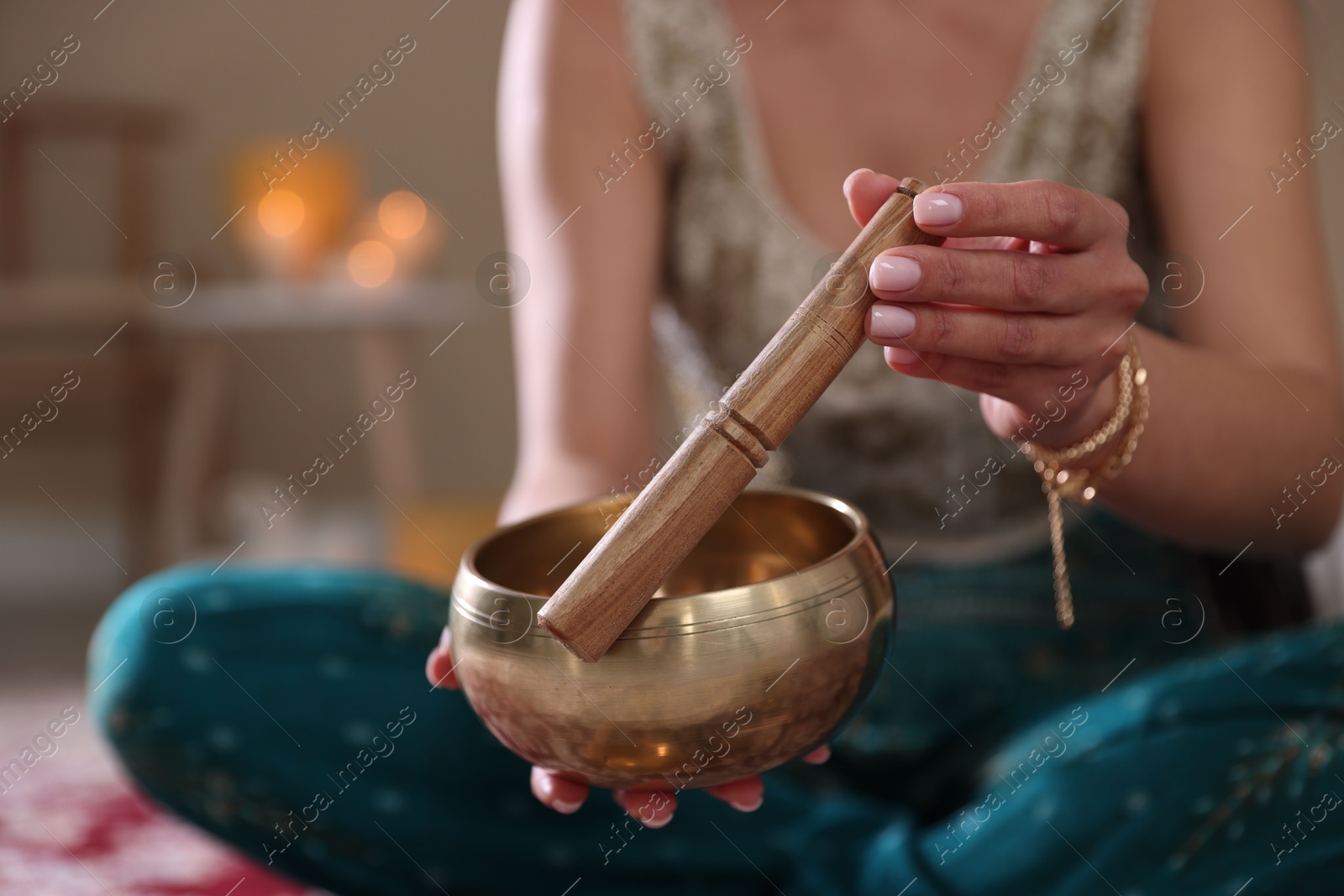 Photo of Woman with singing bowl and burning candles indoors, closeup