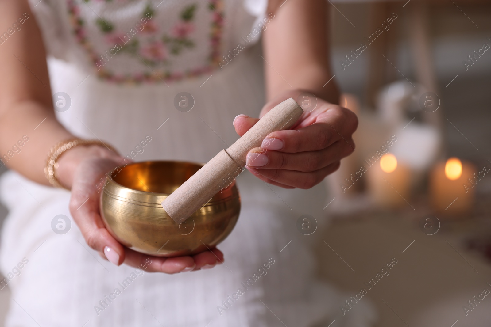 Photo of Woman with singing bowl and burning candles indoors, closeup