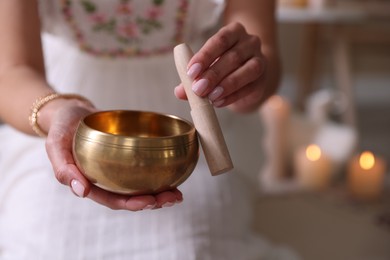 Photo of Woman with singing bowl and burning candles indoors, closeup