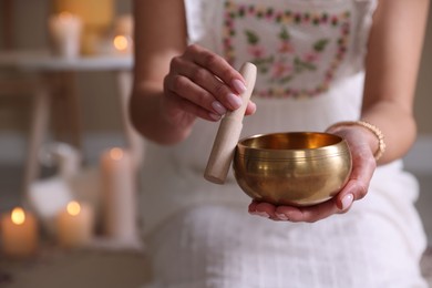 Photo of Woman with singing bowl and burning candles indoors, closeup