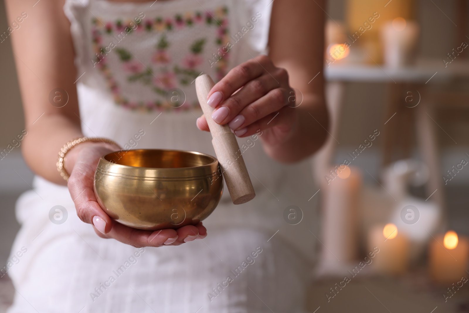 Photo of Woman with singing bowl and burning candles indoors, closeup