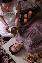 Woman undergoing singing bowl therapy indoors, top view