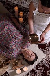 Woman undergoing singing bowl therapy indoors, top view