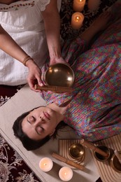 Woman undergoing singing bowl therapy indoors, top view